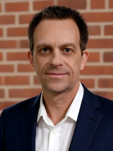 Neil Monroe headshot with a red brick background